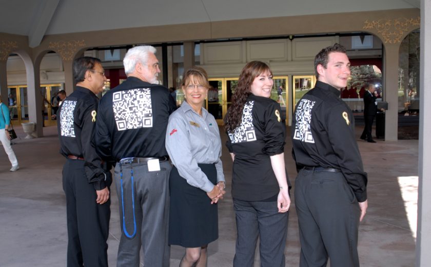 three men and one woman wearing all black dress shirts and pants, one woman wearing blue shirt and black skirt