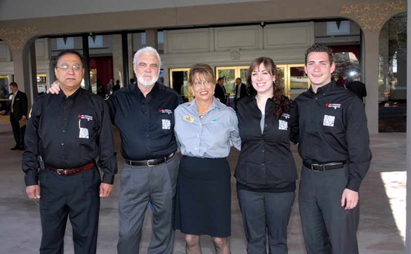 three men and one woman wearing all black dress shirts and pants, one woman wearing blue shirt and black skirt