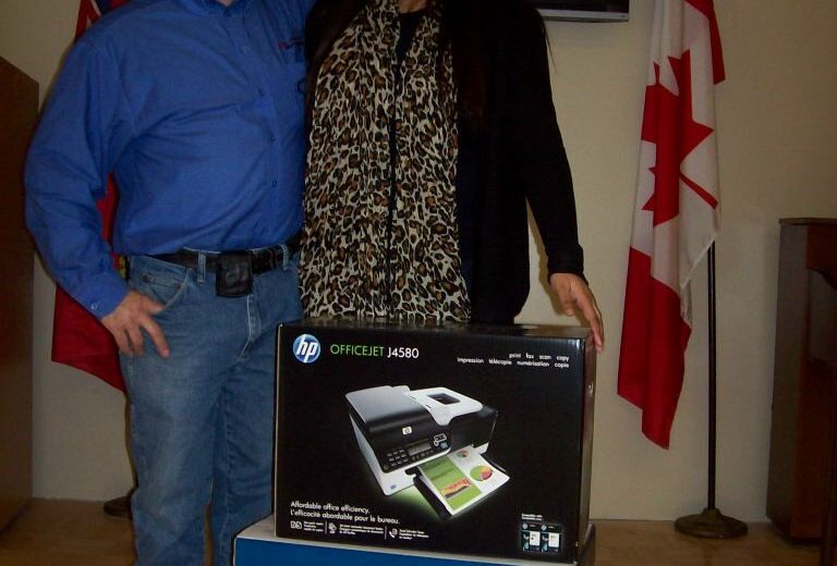 man wearing blue shirt and blue jeans next to woman wearing leopard print shirt and black sweater, black tv hanging on wall, red and white Canadian Flag, black and blue boxes in the front