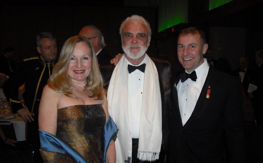 Garrison Officer's Ball, green lighting, two men wearing black and white suits, women wearing gold and blue dress