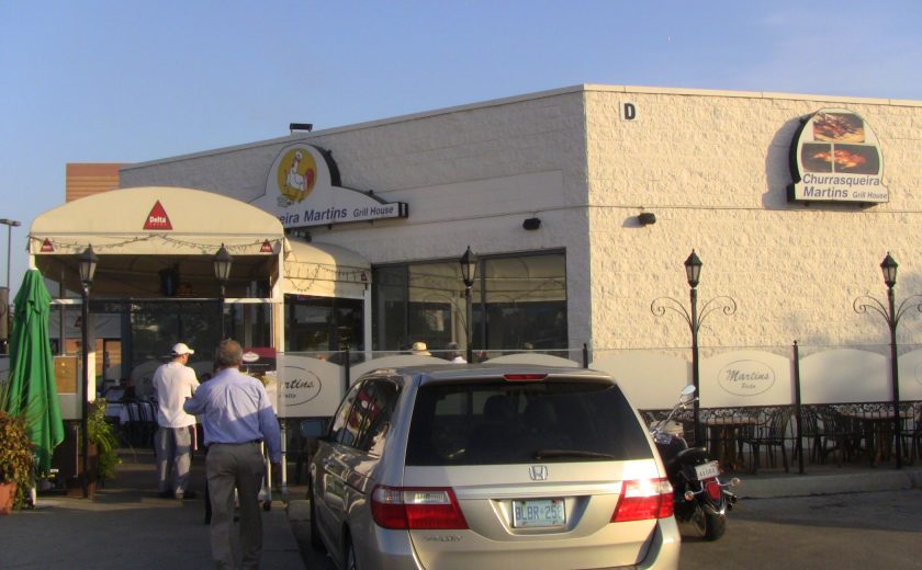 white building with a tent roof as the entry way, beige car and black motorcycle in the front, people walking into the building