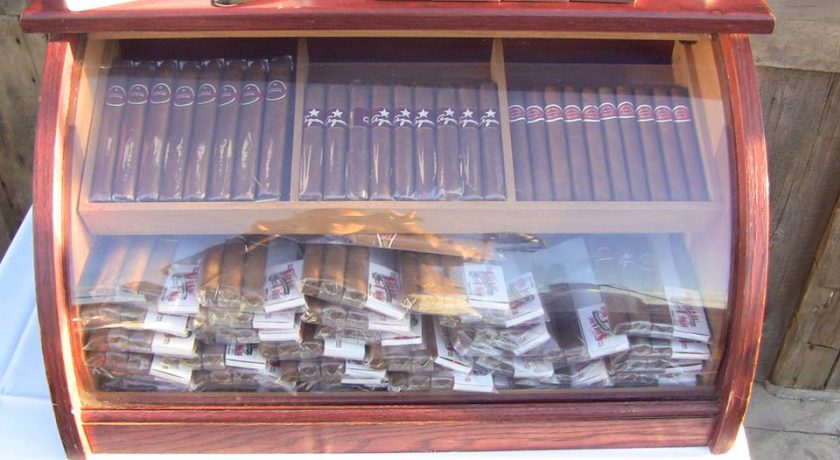 mahogany case with glass front full of packs of brown cigars sitting on a white table