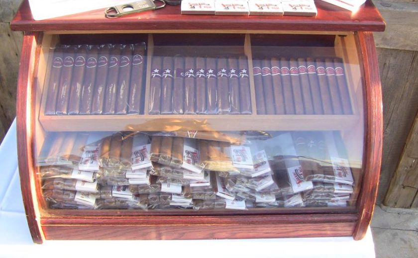 mahogany case with glass front full of packs of brown cigars sitting on a white table