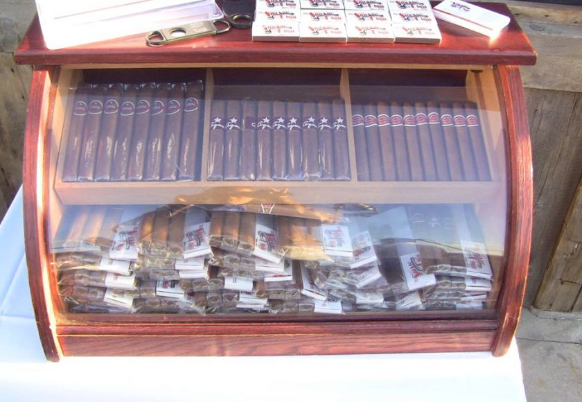 mahogany case with glass front full of packs of brown cigars sitting on a white table