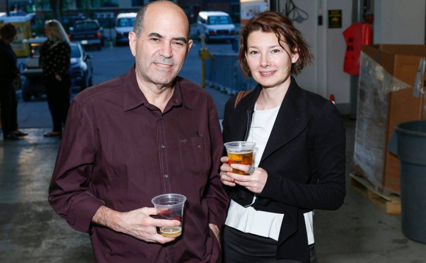 man wearing maroon shirt and woman wearing white shirt with black jacket, inside self storage facility, parking lot filled with cars in the background