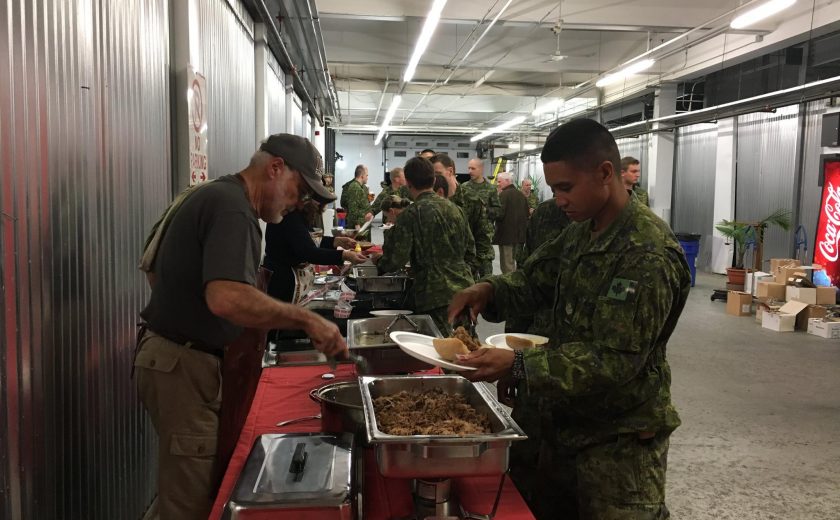 group of men wearing green army uniforms lining up to get food from silver containers