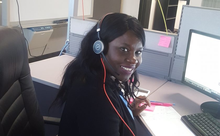 Women wearing black and a headset in front of a computer in the client management office, pink and green balloon in the background