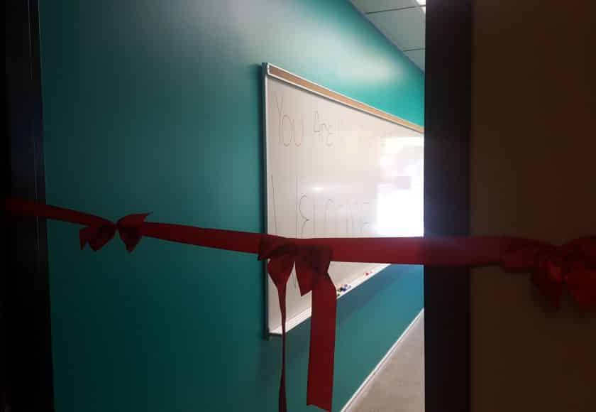 long red ribbon with three bows across open client management office door, teal coloured wall with whiteboard hanging