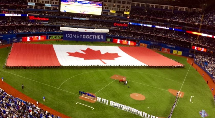 full baseball stadium filled with people, large red and white Canadian flag with the red maple leaf in the middle, baseball players lined up