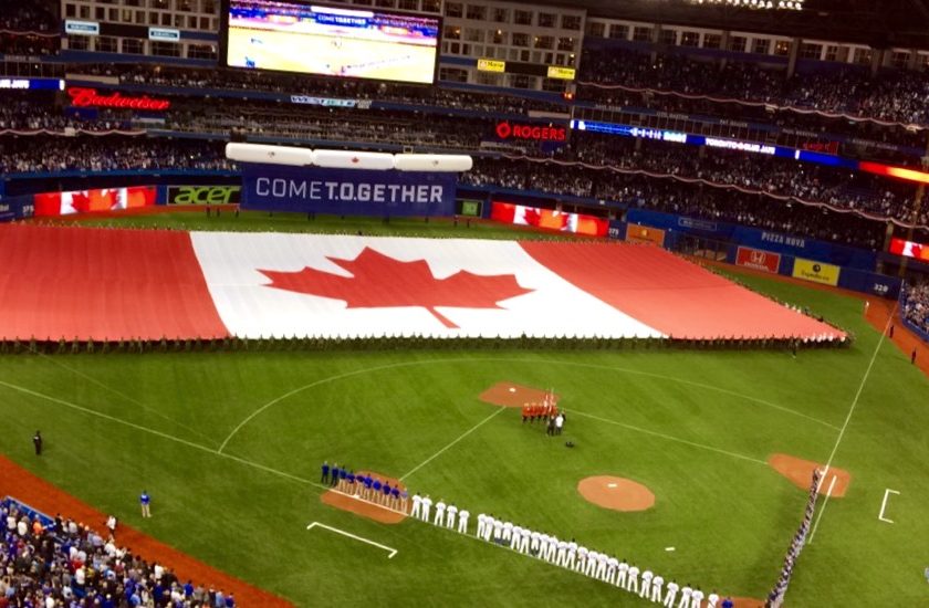 full baseball stadium filled with people, large red and white Canadian flag with the red maple leaf in the middle, baseball players lined up