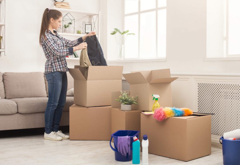 lady wearing plaid shirt and blue jeans packing belongings in brown boxes in white room