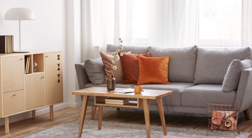 Retro wooden coffee table in front of grey couch in classy living room interior