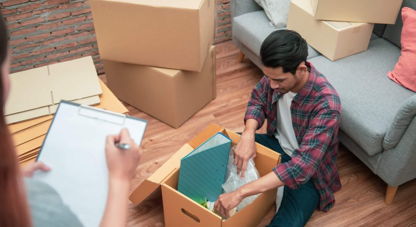 Young Asian couple packing their belonging into cardboard box by using a check list before moving to new resident or house after buy or rent a new one.