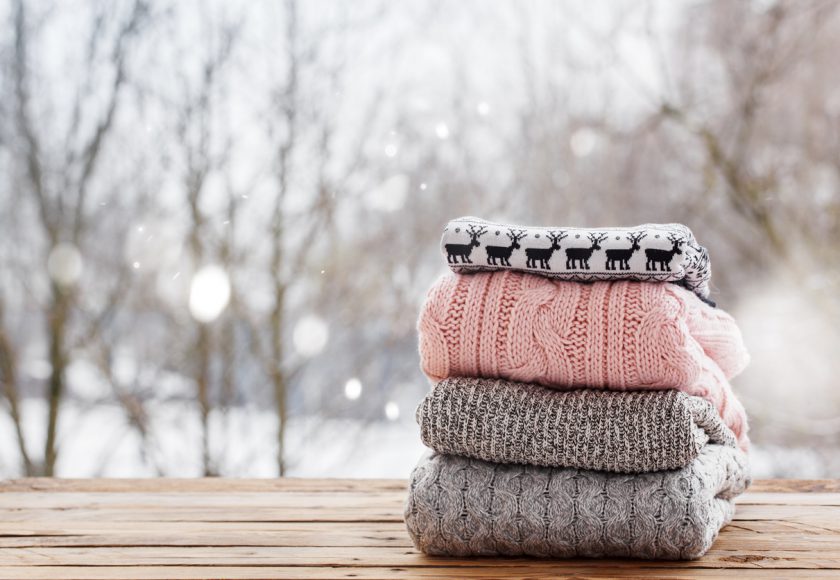 Stack of knitted sweaters on wooden tableon winter nature background.