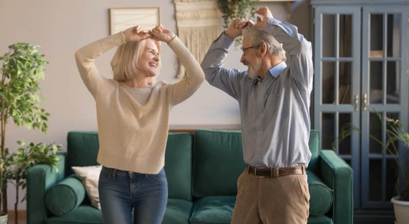 Funny sixty years old couple in love having fun at home, elderly spouses standing raised hands dancing feels carefree healthy enjoy active weekend, do exercises well being of retirees people concept