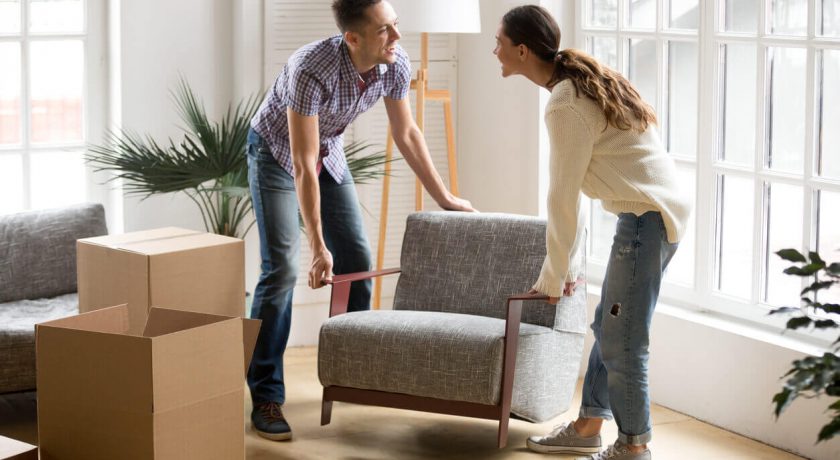 Smiling couple carrying modern chair together placing furniture moving into new home, young family discussing house improvement interior design while furnishing living room, remodeling and renovation