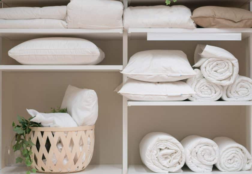 Various household items such as pillows and quilts standing in the white cupboard in the laundry room.